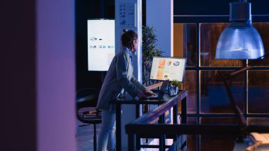 Genç iş kadını geceleri mali raporları analiz ediyor, şirket ofisinde ekonomi grafik analizi üzerinde çalışıyor. Şirket çalışanı kar veya yatırımı artırmak için veri istatistiklerini kontrol ediyor.