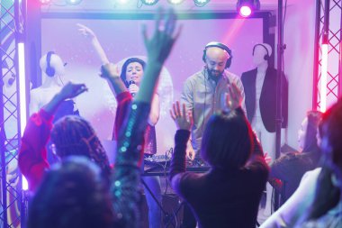 Gece kulübündeki grup konserinde kalabalık dans edip el kaldırıyor. Sahnede sahne alan şarkıcı ve DJ 'ler ve dans pistindeki diskotekte eğlenen farklı insanlar.
