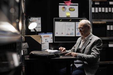 Üst düzey işadamı laptopunu ofis çantasına koyup işten çıkmaya hazırlanıyor. Muhasebe şirketi dosya deposunda muhasebe yöneticisi