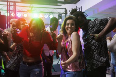 Gece kulübünün dans pistinde erkek arkadaşıyla dans eden gülümseyen kadın spot ışıklarıyla aydınlatılmış. Neşeli, tutkulu, çeşitli çiftler eğleniyor ve kalabalık bir kulüpte müzik ritmine ayak uyduruyorlar.