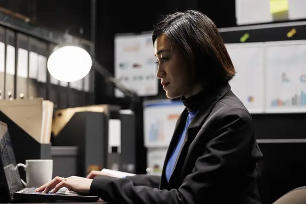 Professional businesswoman checking administrative analytical data in dark file room surrounded by accountancy statistic flowcharts. Asian worker in bureaucratic office filled with invoice folders