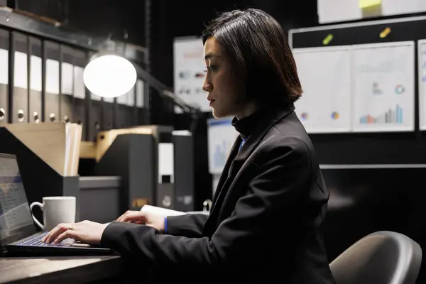 Professional businesswoman accountancy executive adding budget plan data on laptop. Asian woman in file cabinet office filled with paperwork document folders and graphic reports