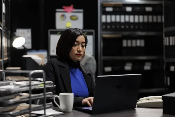 Professional asian accountant checking administrative analytical data on laptop in cabinet office surrounded by accountancy statistic reports. Businesswoman in file storage room