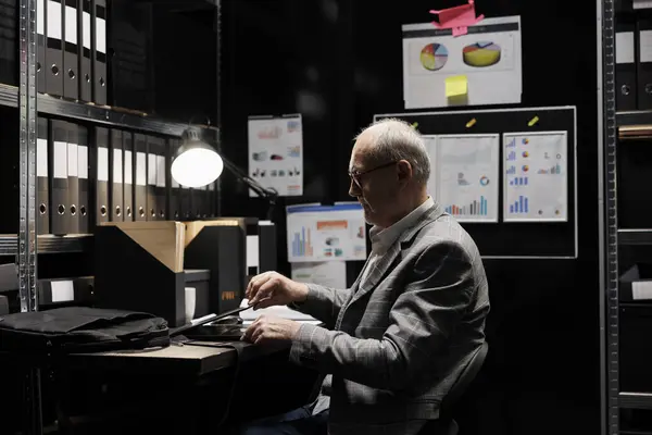 Elderly businessman shutting off laptop at job preparing to leave workplace. Management accounting executive surrounded by financial file statistics data flowcharts in storage room