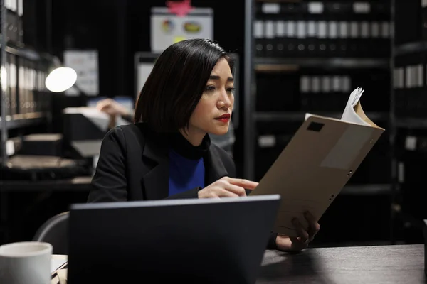Asian businesswoman executive checking accountancy budget plan data paperwork. Bureaucratic administration employee in repository filled with document folders and graphical chart reports