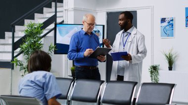 Doktor, hastanenin bekleme salonunda sağlık kontrolünde yaşlı hastaya hastalık teşhisi koyuyor. Yaşlı bir adam sağlık sigortası belgeleri, ilaç hizmetleri dolduruyor.