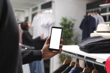 Giyim mağazası müşterisi butik uygulaması için akıllı telefon boş beyaz ekran modeli gösteriyor. Marka tanıtımı için alışveriş merkezi müşterisi cep telefonunu elinde tutuyor.