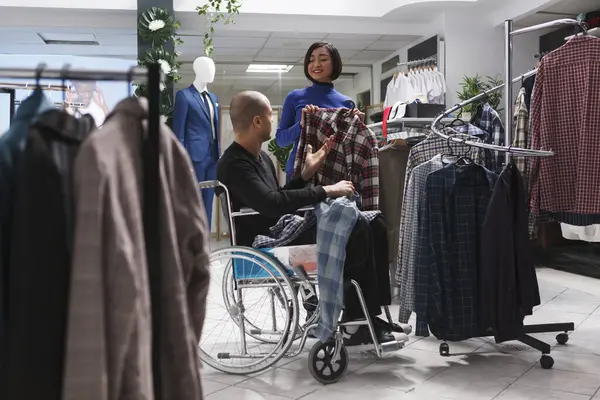 モールブティック笑顔のアジア女性アシスタントは カジュアルな服を選択する身体障害を持つ顧客を支援します 車椅子でバイヤーにアドバイスを提供する部門センター衣料品店 — ストック写真