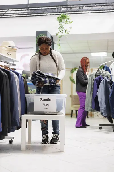 African american customer donating clothes to welfare organization in shopping center. Woman putting new and second hand apparel in donation box while shopping in trendy store