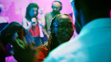 Partide dans figürleri gösteren insanlar, gece kulübünde müzik dinleyen birden fazla insan. Genç yetişkinler diskotekte eğleniyor, dans pistinde parti yapıyorlar. El kamerasıyla..