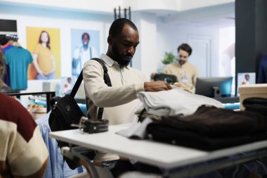 Butik erkek giyim reyonunda giysi inceleyen Afrikalı Amerikalı bir adam, günlük kıyafet arıyor. Müşteri alışveriş merkezinden alışveriş yaparken modaya uygun kıyafetler seçiyor