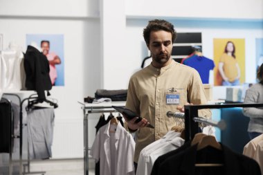 Giyim mağazası asistanı dijital tablette envanter kontrolü yapıyor ve giyim raflarını inceliyor. Alışveriş merkezi çalışanı butik web sitesinde hisse senedi yönetiyor ve askılarda giysi inceliyor.