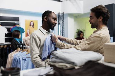 Giysi mağazası çalışanı ve müşteri kontrol tişörtü ve kravat tarzı eşleşme. Alışveriş merkezi butiği resmi giysiler ve müşteri vücuduna aksesuar sunuyor, moda tavsiyeleri sunuyor.