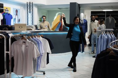 Mutlu Asyalı kadın gülüyor, giysi mağazasından alınmış kıyafetlerle alışveriş torbaları tutuyor. Alışveriş merkezi, butikte kağıt paketlerle gezen neşeli müşterileri tatmin ediyor.