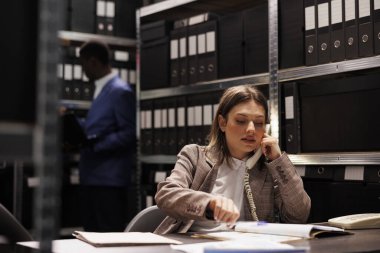 Polis memuru uzaktan kumandalı polis memuruyla konuşmak için sabit telefonu kullanıyor, arşiv odasında olay yeri kanıtlarını tartışıyor. Kriminoloji raporunda fazla mesai yapan özel dedektif davayı çözmeye çalışıyor.