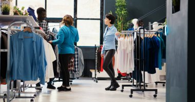Zarif gömlek almak için alışveriş yapan şık bir çift modern butikten almadan önce kıyafet malzemelerini analiz ediyor. Giyim mağazasında yeni moda koleksiyonu olan şık müşteriler askılara bakıyor.