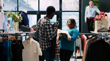 Neşeli çift şık mallarla oynuyor modern butikte modaya uygun kıyafetlerle oynuyorlar. Afrikalı Amerikalı müşteriler yeni gardırop için şık eşyalar alıyorlar. Moda konsepti