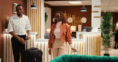 Dost canlısı Asyalı resepsiyonist misafirlere rezervasyon için yardım ediyor, onları şık bir otel salonunda beklemeye davet ediyor. Mutlu konuklar odalarında kontrol edilmeye hazır.