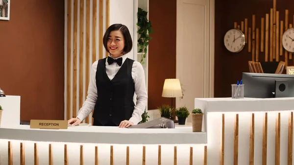 Smiling professional hotel employee taking phone calls while working at reception desk. Happy cheerful receptionist taking booking requests standing at check in counter in welcoming resort lobby