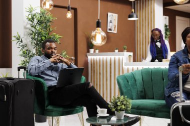 İş için seyahat eden yorgun Afrikalı Amerikalı girişimci otel lobisinde dizüstü bilgisayarla oturup e-postaları kontrol ediyor. Zenci serbest çalışan biri, kayıt için beklerken uzaktan çalışıyor.