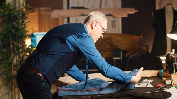 男性のテーラーメイドは高級アトリエで働き ワークステーションで生地を測定します 現代的な服 手作りの針仕事の概念を作成するためにスケッチを分析する経験豊富なクーリエ 手持ち撮影 — ストック写真