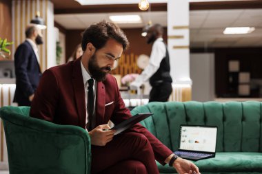 İşadamı otel lobisinde tablet kullanıyor, önemli bir toplantı için yeni fikirler sunuyor. Çalışan, yönetim kurulunu etkilemek için profesyonel bir konuşma yapmaya çalışıyor..