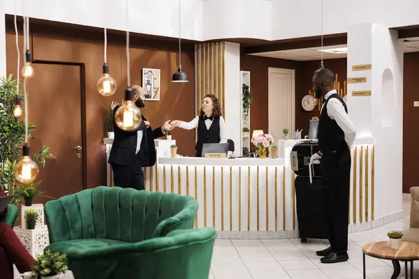 Hotel staff gives access key card to businessman travelling for work, doing check in and preparing for meeting. Entrepreneur in suit talking to front desk receptionist in lobby.