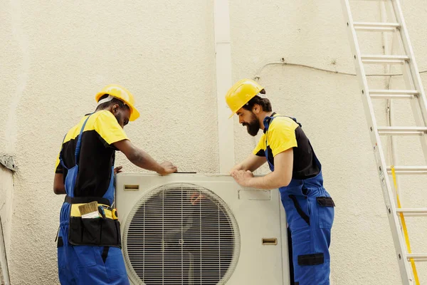 stock image Expert master technician and apprentice serviceman dismantling old busted external air conditioner to replace it with new performant hvac system after draining refrigerant and replacing ductwork