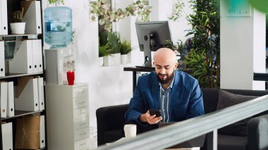 İşteyken akıllı telefon kullanan bir girişimci, araştırma projesi için istatistikleri incelemeden önce çalışma alanında oturuyor. İş ortaklığı kayıtlarını bulmak için cihazla çalışan bir analist. Üçayak atışı.