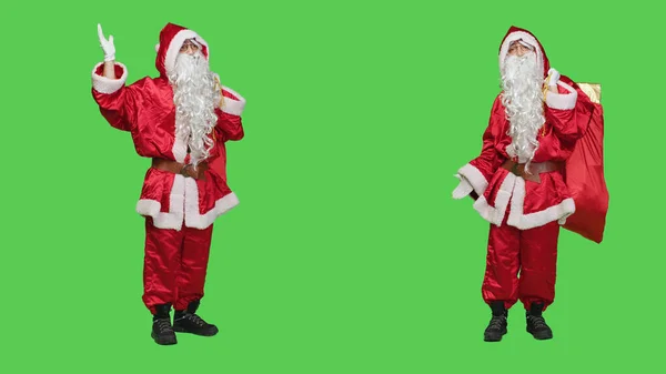 Saint nick creating marketing ad in studio, working on christmas eve holiday advertisement to spread december spirit. Person in santa suit pointing left and right to advertise something.