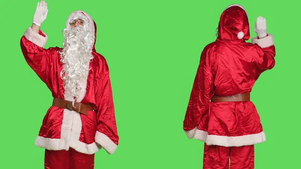 サンニックでは お祝いの季節の衣装を着て グリーンスクリーンを背景にこんにちはを振って 人々を迎えることができます 若いです大人祝うクリスマスの前夜で赤スーツ 笑顔でカメラ — ストック写真