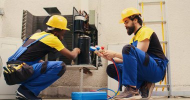 African american repairman cleaning condenser internal components of dirt while coworker assembles professional manifold meters to check freon levels in hvac system