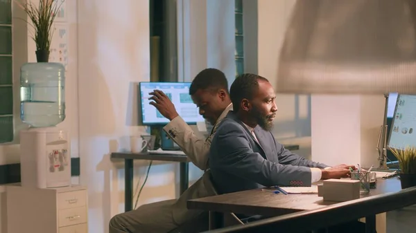 アフリカ系アメリカ人の従業員は 夜勤中に仕事を楽しみ 机の椅子を使って同僚にぶつかりました 友人はオフィスで一晩滞在中に退屈を避けるために互いにレース — ストック写真