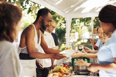 Çeşitli gruplar, evsiz bireylerin ve mültecilerin barındığı bir barınakta ihtiyaç sahiplerine bağış dağıtılmasına yardımcı oluyor. Hayır işçileri yemek servisi yapıyor ve kar amacı gütmeyen bir gıda bankası aracılığıyla yardım teklif ediyorlar..