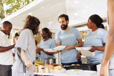 Multiethnic group of volunteers provides aid, handing out free food to disadvantaged communities. They support homeless, sick, and those in poverty. Charitable act of compassion and relief.
