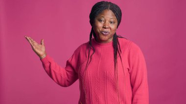 Güzel Afro-Amerikan moda tutkunu canlı pembe gömleği ile etkileyici vücut dilini sergiliyor. Genç siyahi kadın, sağ elini yalıtılmış arka planda gezdiriyordu..