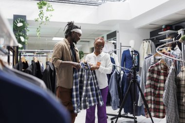 Nüfuzlu ve mağaza müdürü sosyal medya promosyonu için giyim markası sergiliyor. Günlük gömlek gösteren ve akıllı telefon kamerasında erkek giyim koleksiyonundan bahseden blog yazarı ve mağaza asistanı