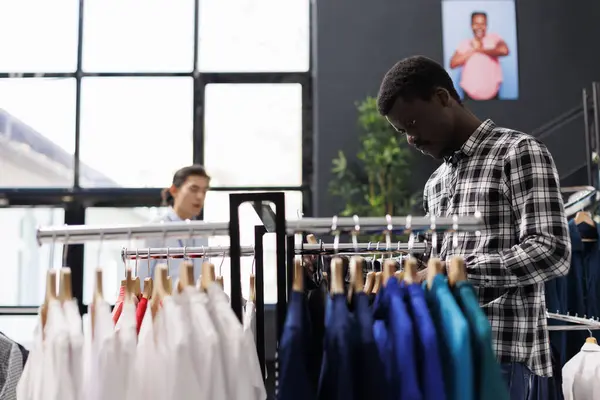 アフリカ系アメリカ人男性の買い物客は カラフルなシャツを見て モダンなブティックでカジュアルなウェアを購入します ファッショナブルな商品の生地と衣料品店の価格をチェックするスタイリッシュな顧客 — ストック写真