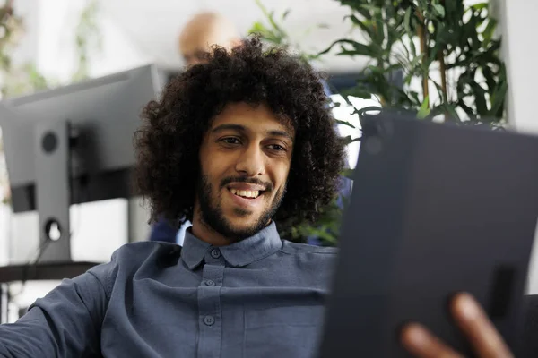 Smiling arab start up company entrepreneur chatting in videocall using digital tablet application. Project manager discussing schedule plan with coworkers in corporate video conference