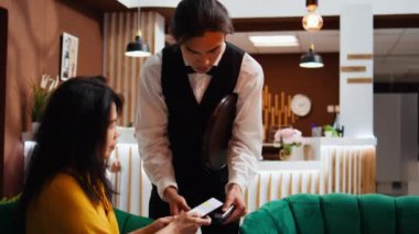 Müşteri, bardan kahve almak için NFC mobil ödemesini kullanıyor. Garson da dinlenme odasında içki servisi yapıyor. Asyalı gezgin otel lobisinde dinleniyor, telefon faturasını pos terminalinde yapıyor, konukseverlik endüstrisinde..