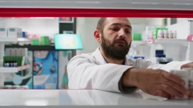 Eczane ürünlerini raflara dizen, müşterilerin ilaç bulabilmesi için stokları sergileyen perakende işçisi POV 'u. Eczacı eczanede ilaç düzenlemeye çalışıyor. Üçayak atışı.