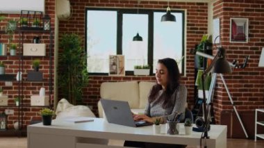 Teleworker dizüstü bilgisayarından e-postalarını kontrol ediyor ve kahvenin tadını çıkarıyor. Evden çalışan, şık, rahat bir dairede çalışan, sıcak içecek içen, kamera A.