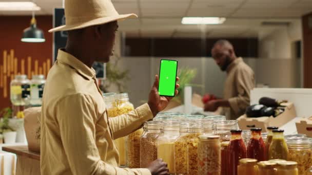 ビジネスオーナーが電話で空白の緑色のディスプレイを提示し 無駄のないエコストアで隔離されたモックアップレイアウトを示しています 携帯電話で染色体テンプレートを使用するアフリカ系アメリカ人ベンダー カメラ — ストック動画