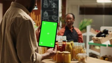 Afro-amerikan müşteriler yerel organik dükkanda yeşil ekran desenli tablet tutuyorlar, katkı maddelerinin yanındaki krom anahtara bakıyorlar. Düzenli müşteri izole edilmiş kopyalama alanı olan bir cihaz kullanır. Kamera A.