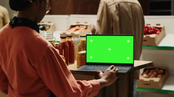 年轻的供应商在为客户准备商品时 在笔记本电脑上看绿屏 在屏幕上使用孤立的模拟布局 非裔美国人卖主检查空白的铬钥匙显示屏 相机A — 图库视频影像