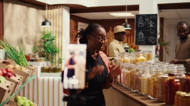 商人在当地农贸市场上制作促销录像带 谈论天然自制食品酱料和食品供应或调味料 从事营销工作的非裔美国妇女 摄像头B — 图库视频影像