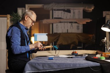 Özel dikim giysi için uygun düğme için dikiş aksesuarları kutusuna bakan yaşlı terzi. Atletizm atölyesinde modaya uygun giyinen deneyimli bir terzi.