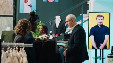 Afro-amerikan mağaza asistanı eski müşteriye gömlek ile kravat uyumu için yardım ediyor, moda galerisinde zarif bir kıyafet yaratıyor. Alışveriş merkezindeki modaya uygun yaşlı müşteriye yardımcı çalışan. Kamera A.