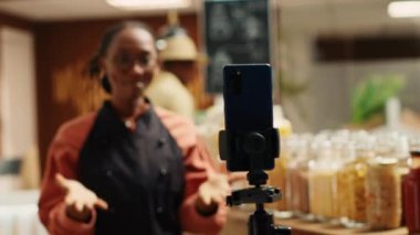 Pazar çalışanı müşterileri çekmek için pazarlama ticari videosu yaratıyor, yeniden kullanılabilir kavanozlarda ücretsiz kiler ve yerel olarak yetişmiş ürünler için katkı maddeleri tanıtıyor. Biyolojik ürünleri sunan kadın. Kamera A.