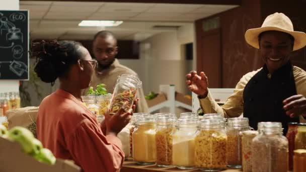 农民与围裙推荐新的自制酱汁的妇女 显示有机面食类型和其他食品供应 非洲裔美国人卖主向常客介绍产品 相机A — 图库视频影像
